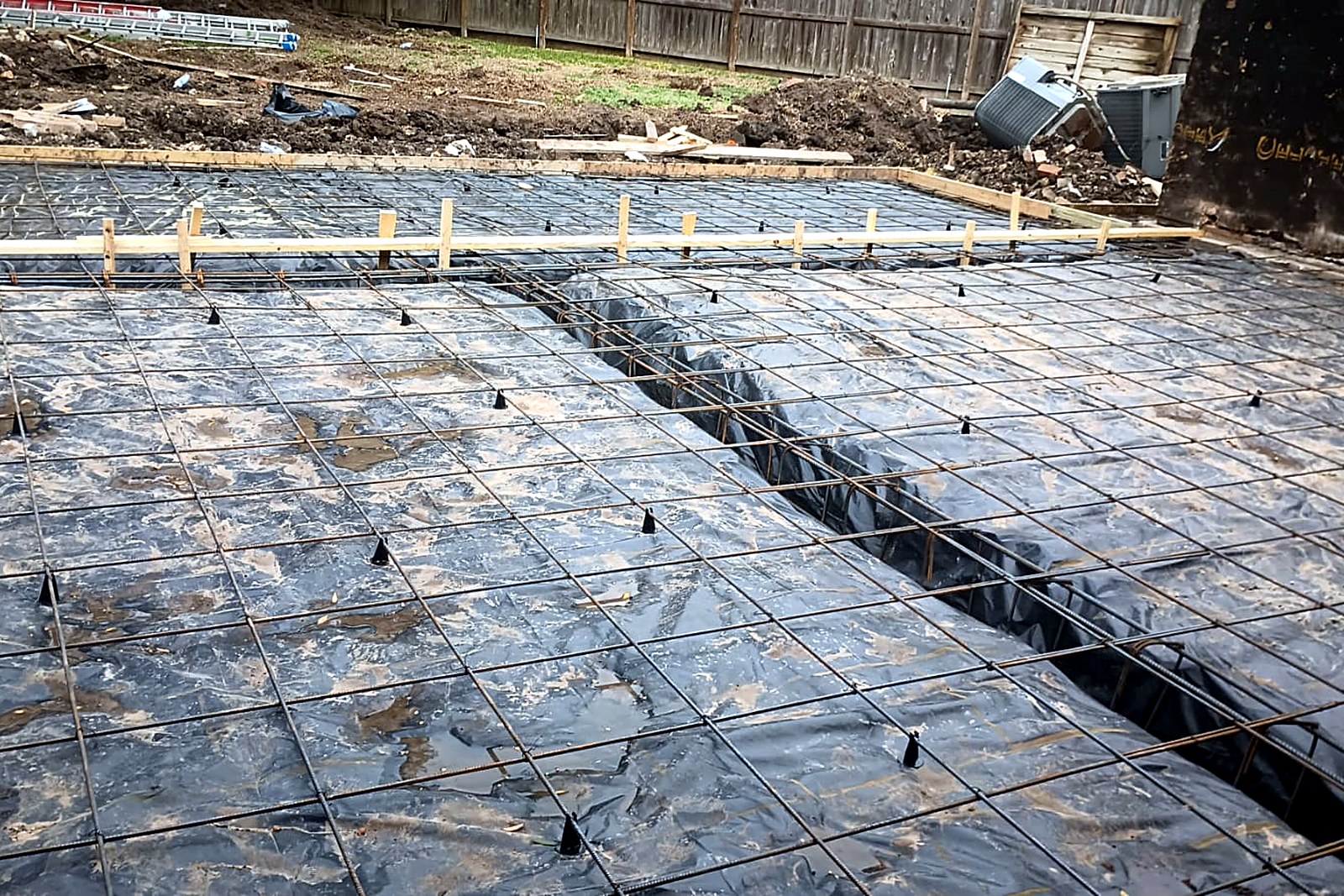 Foundation rebar grid supported on chairs above a black vapor barrier