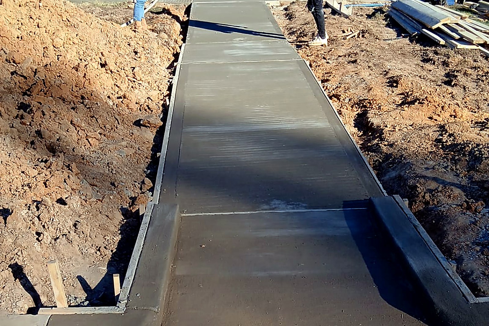 Long wet concrete sidewalk run being finished with a curb transition