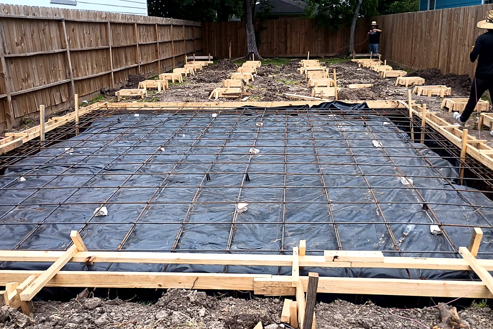 Concrete foundation forms with a rebar grid over a black vapor barrier