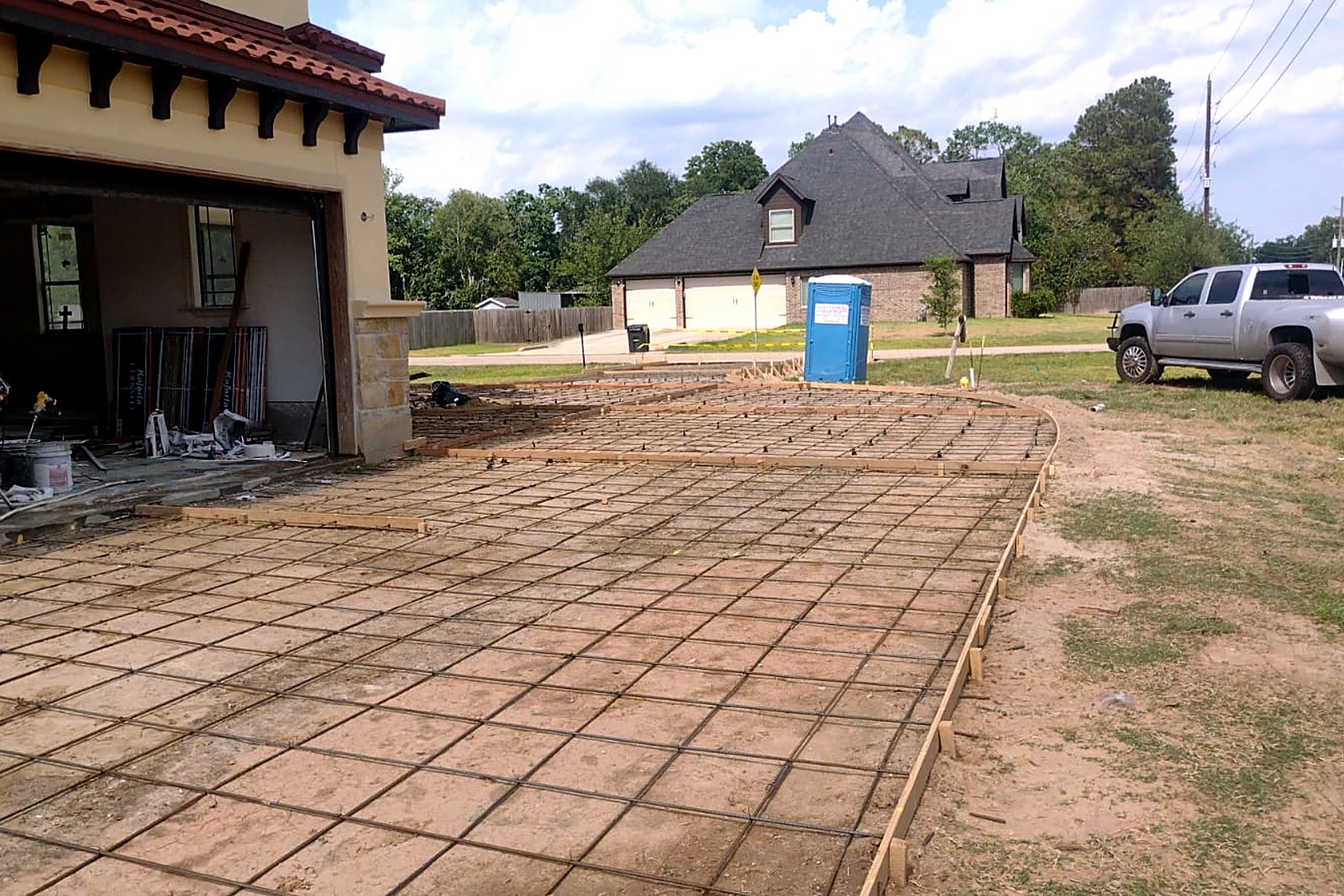 Rebar grid set inside curved wooden driveway forms near a residential garage