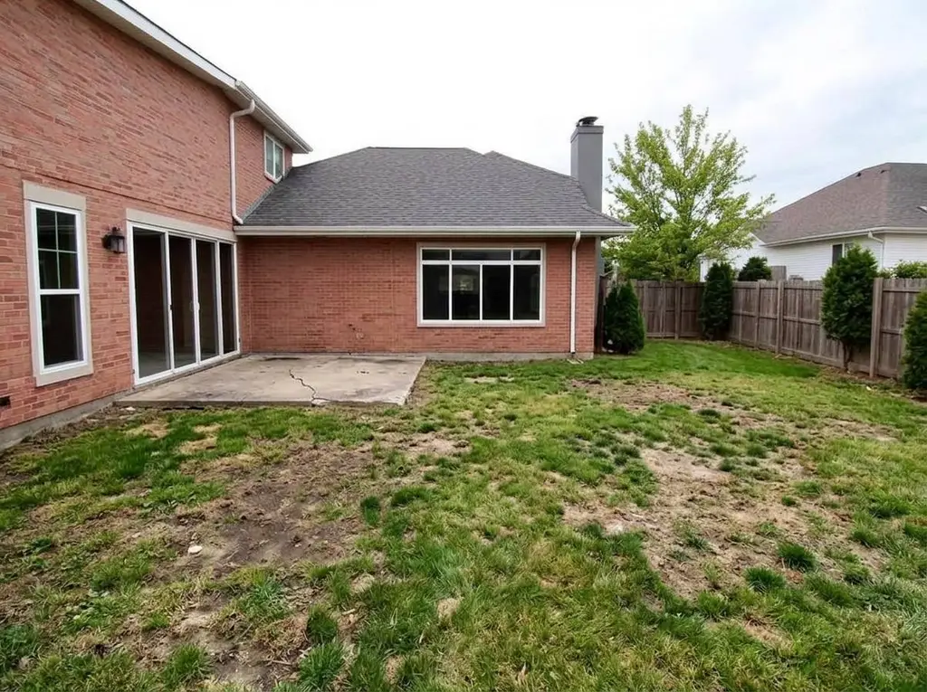 Brick home backyard with patchy grass and a small cracked slab before patio work
